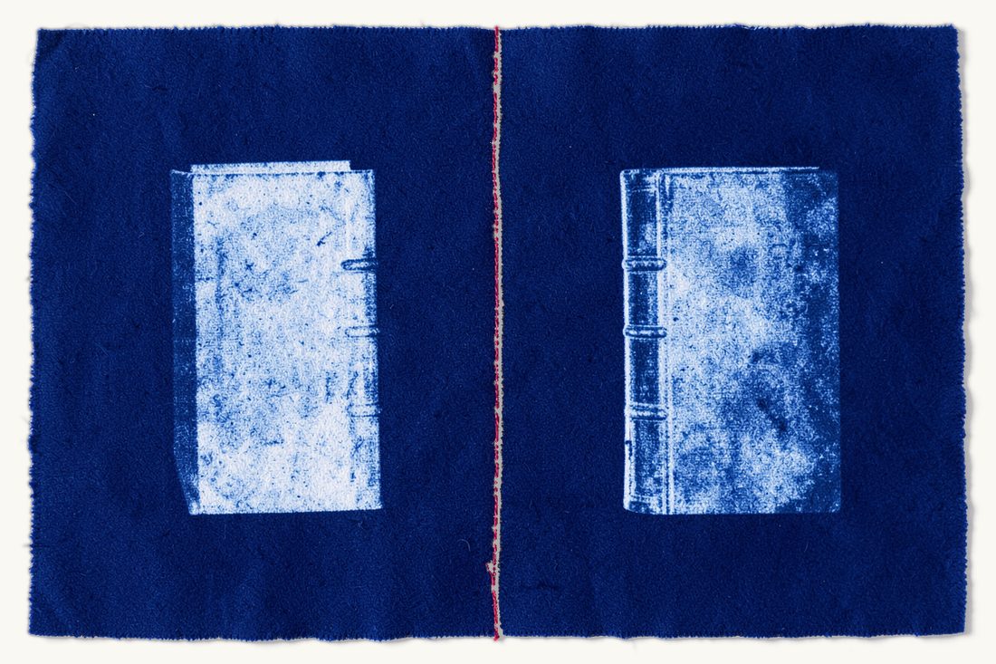 Cyanotype print: two identical silhouettes of a thick antique book mirrored on either side of a vertical red thread